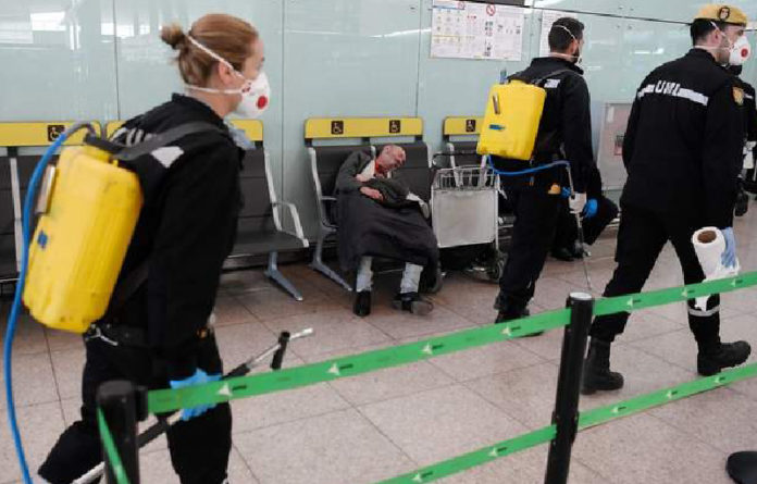 Un hombre duerme mientras una Unidad Militar de Emergencias se prepara para desinfectar el aeropuerto de El Prat de Llobregat, en Barcelona, España. Foto Afp.