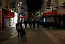 Una mujer con tapaboca camina por las calles den París, dándole la espalda a cuatro policías. Foto Ap.