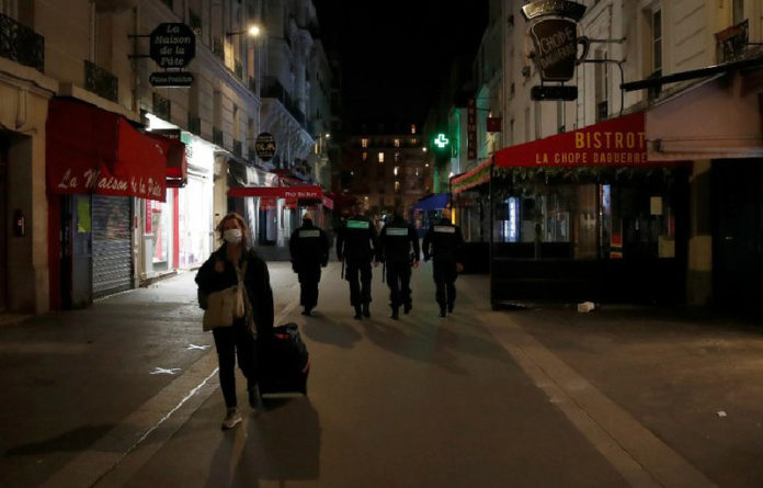 Una mujer con tapaboca camina por las calles den París, dándole la espalda a cuatro policías. Foto Ap.