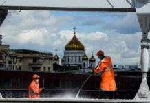 Dos trabajadores desinfectan un puente frente a la catedral del Cristo Salvador, en Moscú, Rusia. Foto Afp.