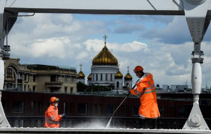 Dos trabajadores desinfectan un puente frente a la catedral del Cristo Salvador, en Moscú, Rusia. Foto Afp.