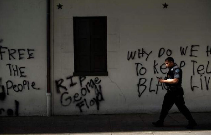 Un miembro del Servicio Secreto de EU pasa junto a un graffiti cerca de la Casa Blanca, tras una noche de protestas por la muerte de George Floyd. Foto Afp.