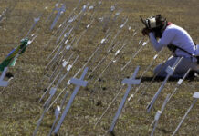 Un manifestante se arrodilla ante cruces que representan los miles de muertos por coronavirus, frente al Congreso de Brasil, en Brasilia. Foto Ap.