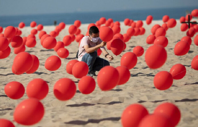 Un hombre coloca globos rojos en la arena de la playa de Copacabana en una manifestación organizada por Río de Paz para honrar a las víctimas del Covid-19. Foto AP.