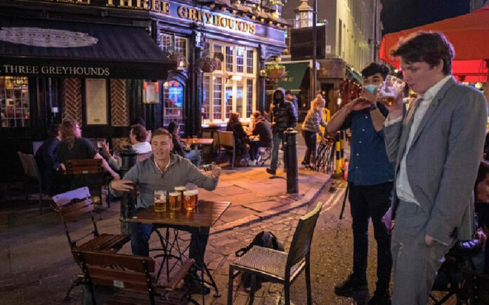 Clientes beben en un ‘pub’ en Londres, Inglaterra, durante el primer día de horario restringido como medida contra la pandemia. Foto Afp.