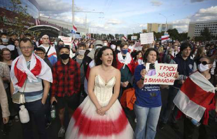 Manifestantes con viejas banderas nacionales bielorrusas, uno con un cartel que dice: 